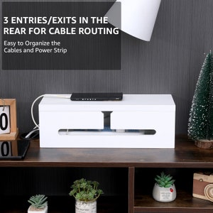 May include: A white cable management box with a black device on top. The box has slots for cable routing and the text "3 ENTRIES/EXITS IN THE REAR FOR CABLE ROUTING" and "Easy to Organize the Cables and Power Strip".