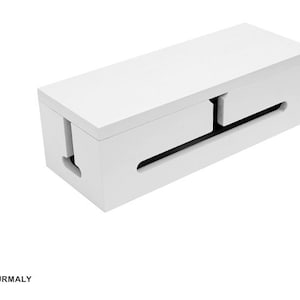 May include: A white rectangular cable management box with a sliding top and slots for cords. The box has a clean, minimalist design, perfect for organizing and concealing cables. The word "TOURMALY" is printed at the bottom.