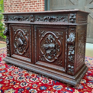 May include: A large, intricately carved wooden sideboard with two doors and three drawers. The doors and drawers feature floral and bird motifs. The sideboard is made of dark wood and has a rich, antique finish.