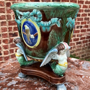 May include: A green and brown ceramic planter with a bird design and two winged mermaids on the base.