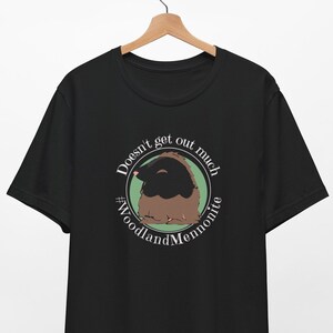 May include: Black t-shirt with a white circle graphic featuring a cartoon mole and the text "Doesn't get out much #WoodlandMennonite"