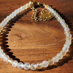 May include: A delicate bracelet made with small, faceted, clear and golden beads. The bracelet has a gold clasp and extender chain.