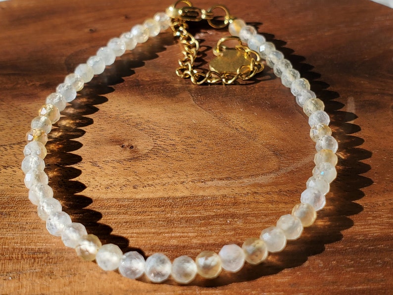 May include: A delicate bracelet made with small, faceted, clear and golden beads. The bracelet has a gold clasp and extender chain.