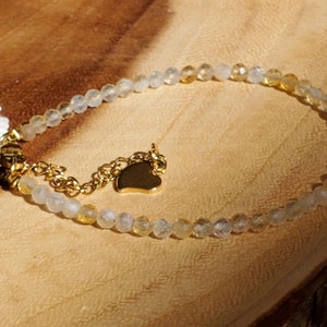 May include: A delicate gold bracelet with clear and yellow beads, a small gold heart charm, and a white flower charm.
