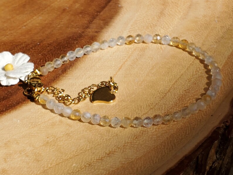 May include: A delicate gold bracelet with clear and yellow beads, a small gold heart charm, and a white flower charm.