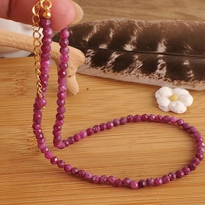 May include: A delicate pink gemstone necklace with a gold clasp. The necklace is made of small, faceted beads and is strung on a thin gold chain.