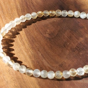 May include: A delicate gold and clear crystal beaded necklace with a gold clasp. The necklace is made of small, faceted beads that are strung together on a thin gold chain.