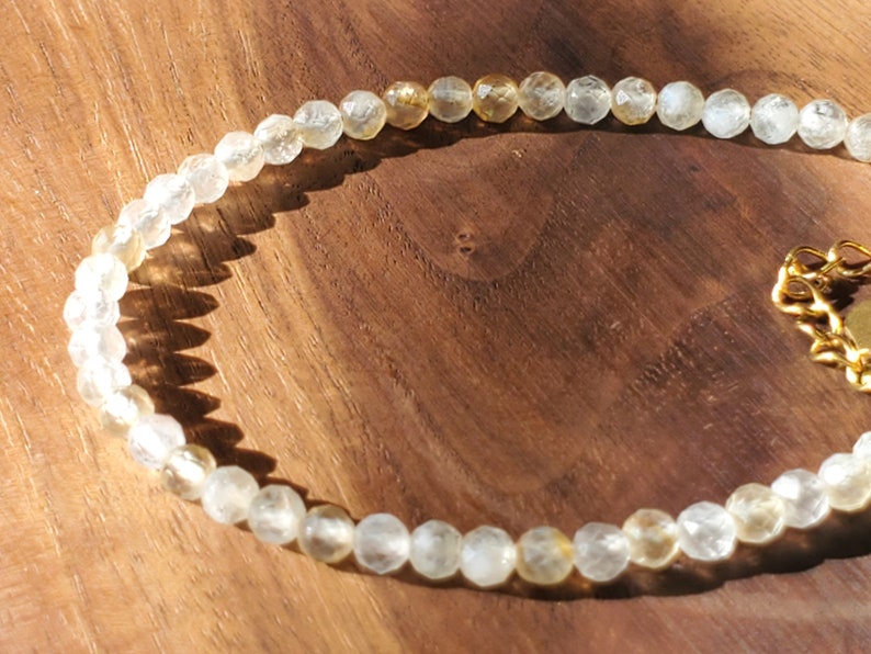 May include: A delicate gold and clear crystal beaded necklace with a gold clasp. The necklace is made of small, faceted beads that are strung together on a thin gold chain.