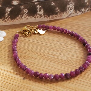 May include: A delicate bracelet made of small, faceted, purple gemstones. The bracelet has a gold clasp and a small heart charm.