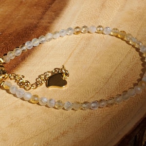 May include: A delicate gold chain bracelet with a heart charm and a mix of clear and yellow beads.