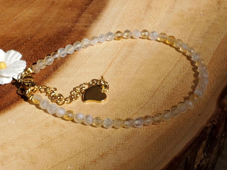 May include: A delicate gold chain bracelet with a heart charm and a mix of clear and yellow beads.