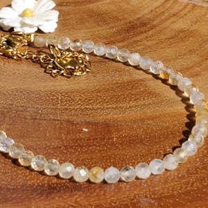May include: A delicate gold chain bracelet with clear and yellow faceted beads. The bracelet has a lobster clasp closure.