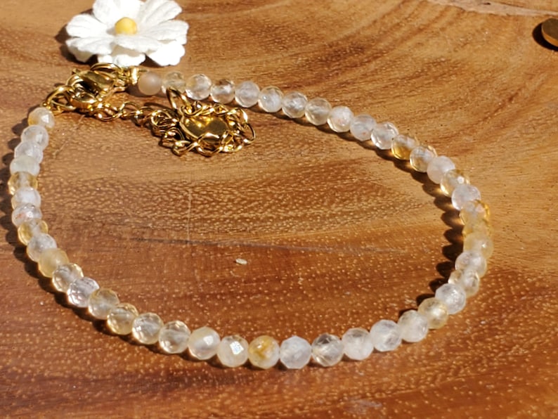 May include: A delicate gold chain bracelet with clear and yellow faceted beads. The bracelet has a lobster clasp closure.