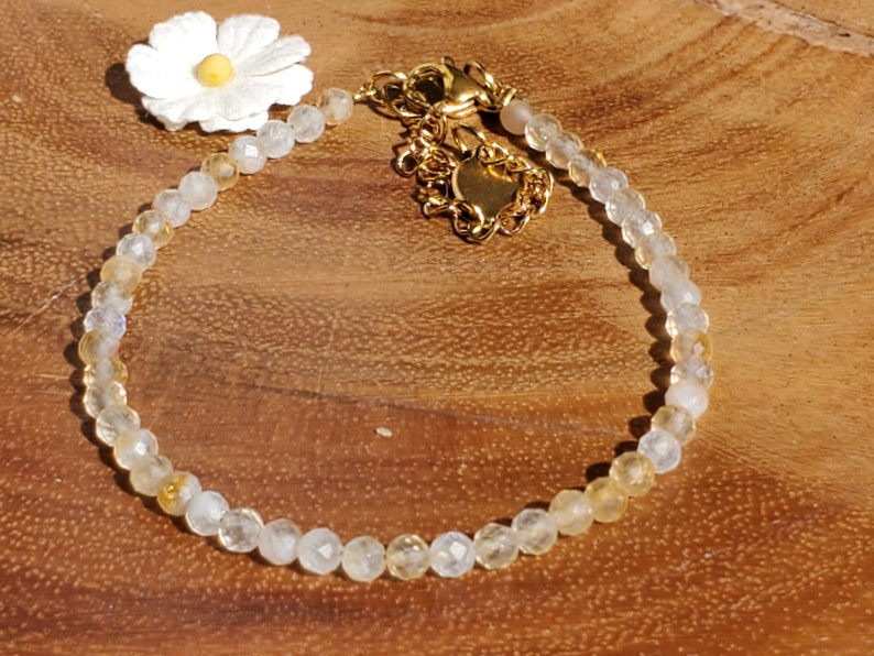 May include: A delicate gold chain bracelet with a white flower charm and clear and yellow beads.
