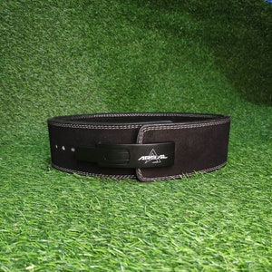 May include: Black weightlifting belt with a white stitched edge and a black buckle with the word "ARESTAL" in white lettering.