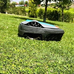 Op de afbeelding: Een grijze en blauwe robotmaaier met zwarte wielen staat op een groen gazon. De maaier heeft een roterend mes.