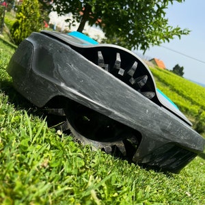Op de afbeelding: Een zwarte en blauwe robotmaaier met een roterende mes. De maaier staat op een groen gazon.