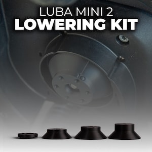 May include: A black "LUBA MINI 2 LOWERING KIT" is shown. The kit contains several black, conical components of different sizes, designed to lower a device. The components are arranged in a row, with a larger device component in the background.