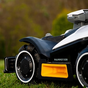 Puede incluir: Primer plano de un cortacésped robótico en blanco y negro con un acento amarillo. El cortacésped tiene un diseño elegante con una parte superior blanca y ruedas negras. El texto "MAMMOTION" es visible.
