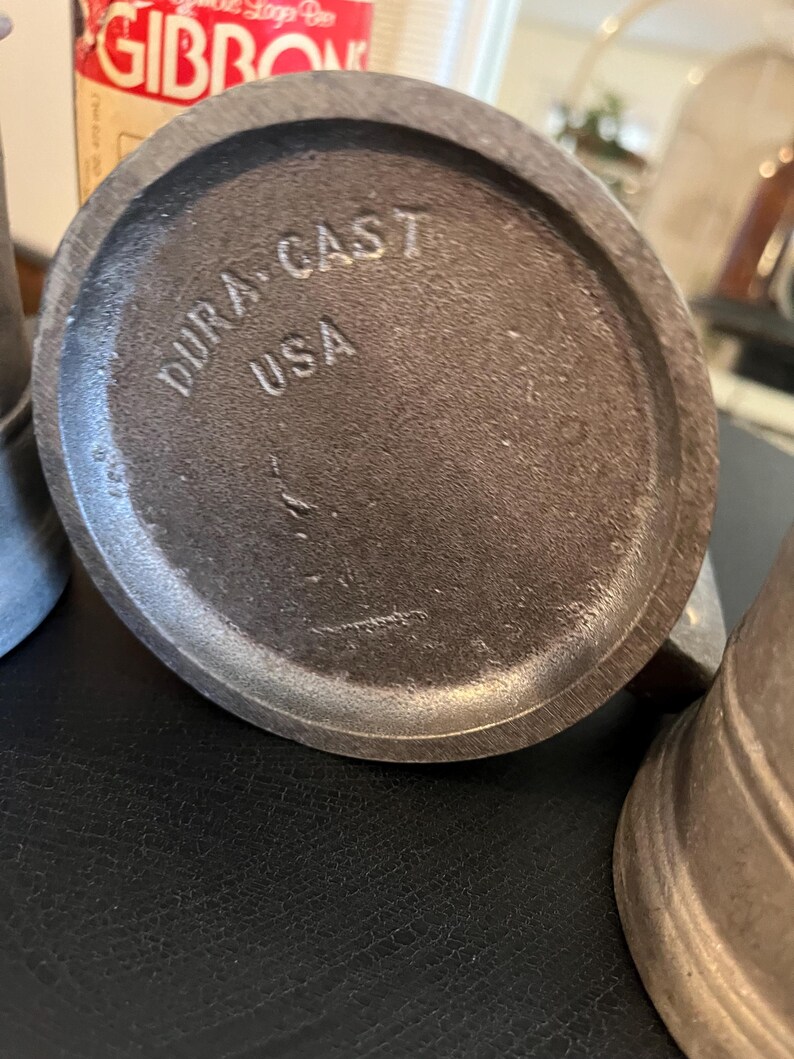 May include: Close-up of the bottom of a metal pitcher with the words "Dura-Cast USA" stamped on the bottom.