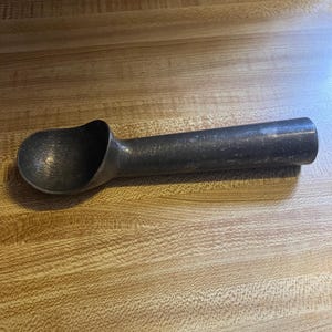 May include: A silver ice cream scoop with a black handle. The scoop is made of metal and has a smooth, shiny finish.