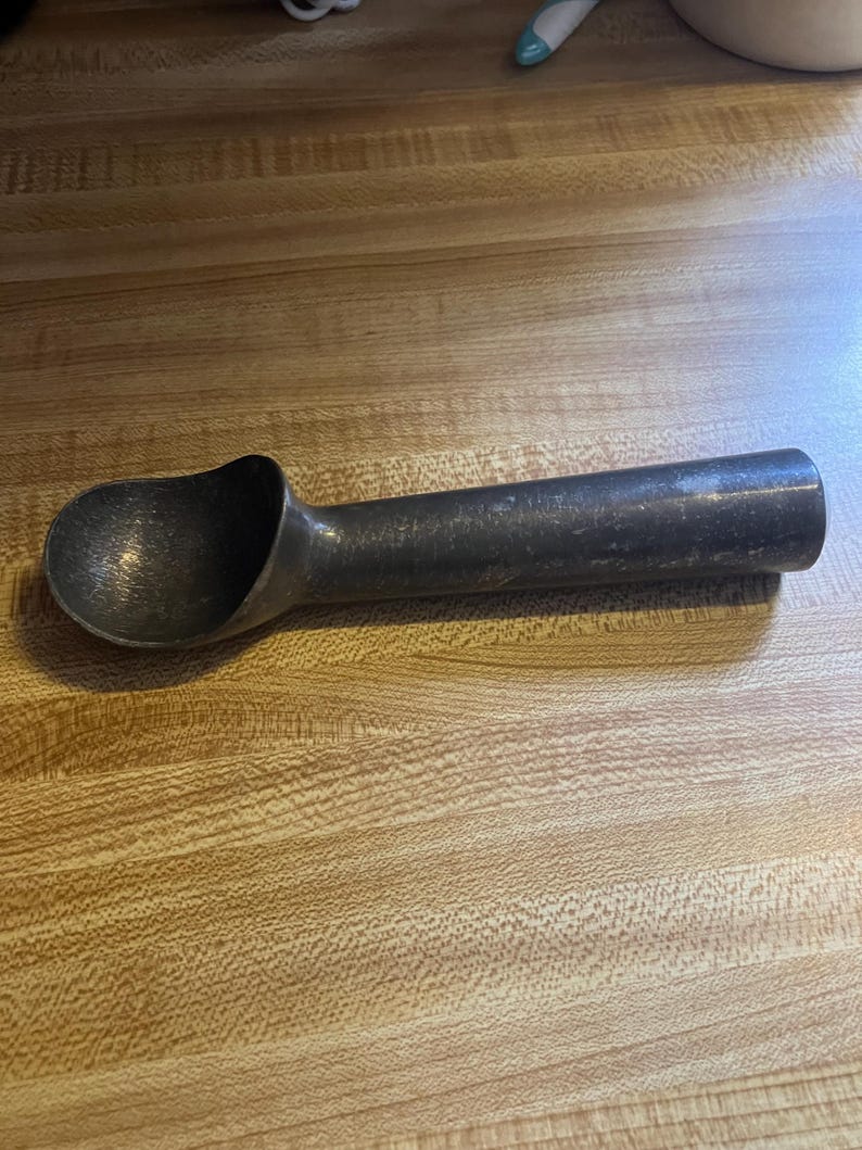 May include: A silver ice cream scoop with a black handle. The scoop is made of metal and has a smooth, shiny finish.