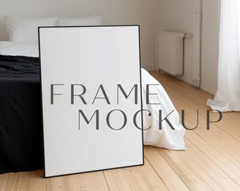 May include: A black frame mockup leaning against a white bed with black and white bedding. The frame is empty and ready for your design.