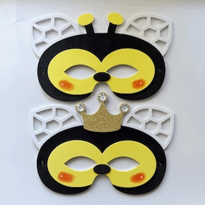 Può includere: Due maschere da ape nere e gialle con ali bianche e una corona dorata. Le maschere hanno occhi gialli e guance arancioni.