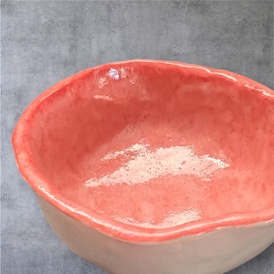 May include: A small, coral-colored ceramic bowl with a slightly uneven rim. The bowl is glazed and has a glossy finish.
