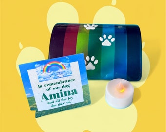 May include: A rainbow-colored glass dog memorial with a paw print design. A card with the text "In remembrance of our dog Amina and all the joy she gave us." and a small white candle are also included.