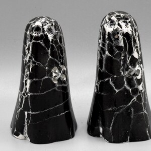 May include: Two salt and pepper shakers with a black and white marble effect. Each shaker has a flared base and a small silver-coloured decorative accent. These are decorative kitchen items.