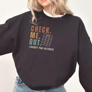 May include: Black sweatshirt with a vintage-style graphic that says "Check Me Out. Library Pun Intended" with a small calendar icon that says "Date".