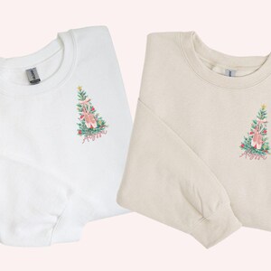 May include: Two long-sleeved sweatshirts with a Christmas tree design featuring ballet shoes and the name "Anya". One sweatshirt is white and the other is beige.