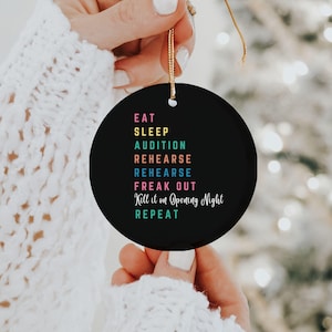 May include: Black round ornament with white text that reads "Eat, Sleep, Audition, Rehearse, Rehearse, Freak Out, Kill it on Opening Night, Repeat". The text is in different colors.