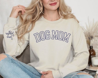 May include: A cream-colored sweatshirt with the text "DOG MOM" in navy blue outlined letters. The sweatshirt has long sleeves and a crew neck.