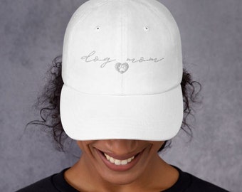 May include: White baseball cap with a paw print heart and the text "dog mom" embroidered in silver thread.