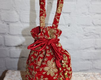 Könnte beinhalten: Roter Samt-Beutel mit goldener Blumenstickerei und passenden Henkeln. Die Tasche hat einen roten Satin-Schleifenverschluss und eine Quaste mit goldenen Perlen. Ein dekoratives und elegantes Accessoire.