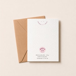 May include: A white greeting card with a textured surface and a brown envelope. The card features a pink circular logo with the text Abbie Lou Doodles, the phrase Doodles Bring Smiles, and the text AbbieLouDoodles - Etsy, @abbieloudoodles, Handmade in the UK.
