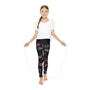 May include: A person wearing black leggings patterned with the word "CLOG" in pink and white. They are holding a jump rope with green handles and a white rope, and are wearing a white crop top.