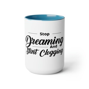 May include: White ceramic mug with a blue interior. The mug features the text "Stop Dreaming And Start Clogging" in black script and sans-serif font. A simple and humorous design for a coffee or tea lover.