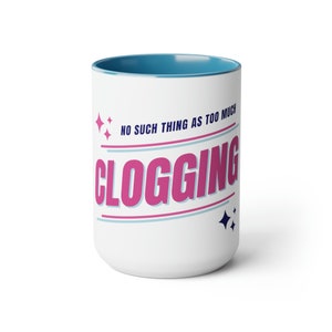 May include: White ceramic mug with a blue rim. The mug has a pink and blue design with the text "NO SUCH THING AS TOO MUCH CLOGGING".