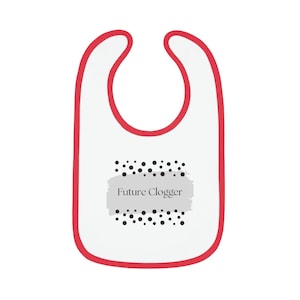 May include: White baby bib with a red trim. The bib features the text "Future Clogger" in a grey rectangle, surrounded by black polka dots. The bib is designed for infants and toddlers.