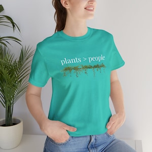 May include: A turquoise blue t-shirt with the text "plants > people" in white lettering. The text is surrounded by a graphic of green vines.