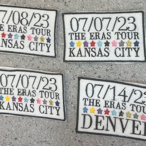 May include: Four white rectangular patches with black borders. Each patch has a date, "THE ERAS TOUR", and a city name: Kansas City or Denver. Colorful star-shaped designs are below the text.