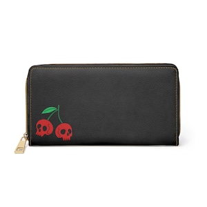 May include: Black wallet with a gold zip and a red cherry skull design. The cherries have a green stem and leaves. The wallet is rectangular and has a smooth texture.