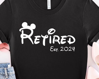 May include: Black t-shirt with white text that says "Retired Est. 2024" with a Mickey Mouse head icon. The shirt is on a white surface with a pair of pink sunglasses and a pair of pink shoes.