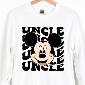 Pu&ograve; includere: Felpa bianca con grafica in bianco e nero di Topolino e la parola "UNCLE" ripetuta in un font retr&ograve;. La felpa ha maniche lunghe e girocollo. La parola "WHITE" &egrave; stampata in alto a sinistra.