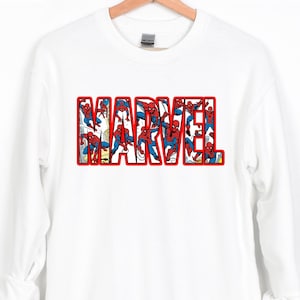 Puede incluir: Sudadera blanca con la palabra "MARVEL" en letras rojas. Las letras est&aacute;n rellenas de im&aacute;genes de Spider-Man con su cl&aacute;sico traje rojo y azul. La palabra "WHITE" est&aacute; en la esquina superior izquierda.