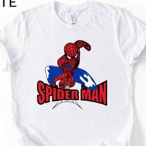 Op de afbeelding: Wit T-shirt met een rode en blauwe Spider-Man afbeelding en de tekst "SPIDER MAN" in het rood. De superheld wordt in een dynamische pose afgebeeld. Het T-shirt heeft een ronde hals.