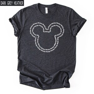 Peut inclure: T-shirt gris fonc&eacute; chin&eacute; avec un motif de t&ecirc;te de Mickey Mouse blanc. Le motif est compos&eacute; du mot "Mickey" r&eacute;p&eacute;t&eacute; en cercle. Le t-shirt est fait d'une mati&egrave;re douce et confortable.
